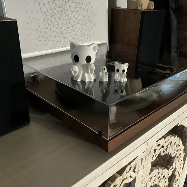 A group of ghost-themed figurines is displayed on the transparent cover of a record player. The arrangement includes two ghost cat figures with large black eyes and draped sheet-like bodies, accompanied by two smaller ghost decorations. The minimalist white design contrasts with the dark surface, creating a playful yet eerie Halloween-inspired setup that doubles as a unique home décor accent.