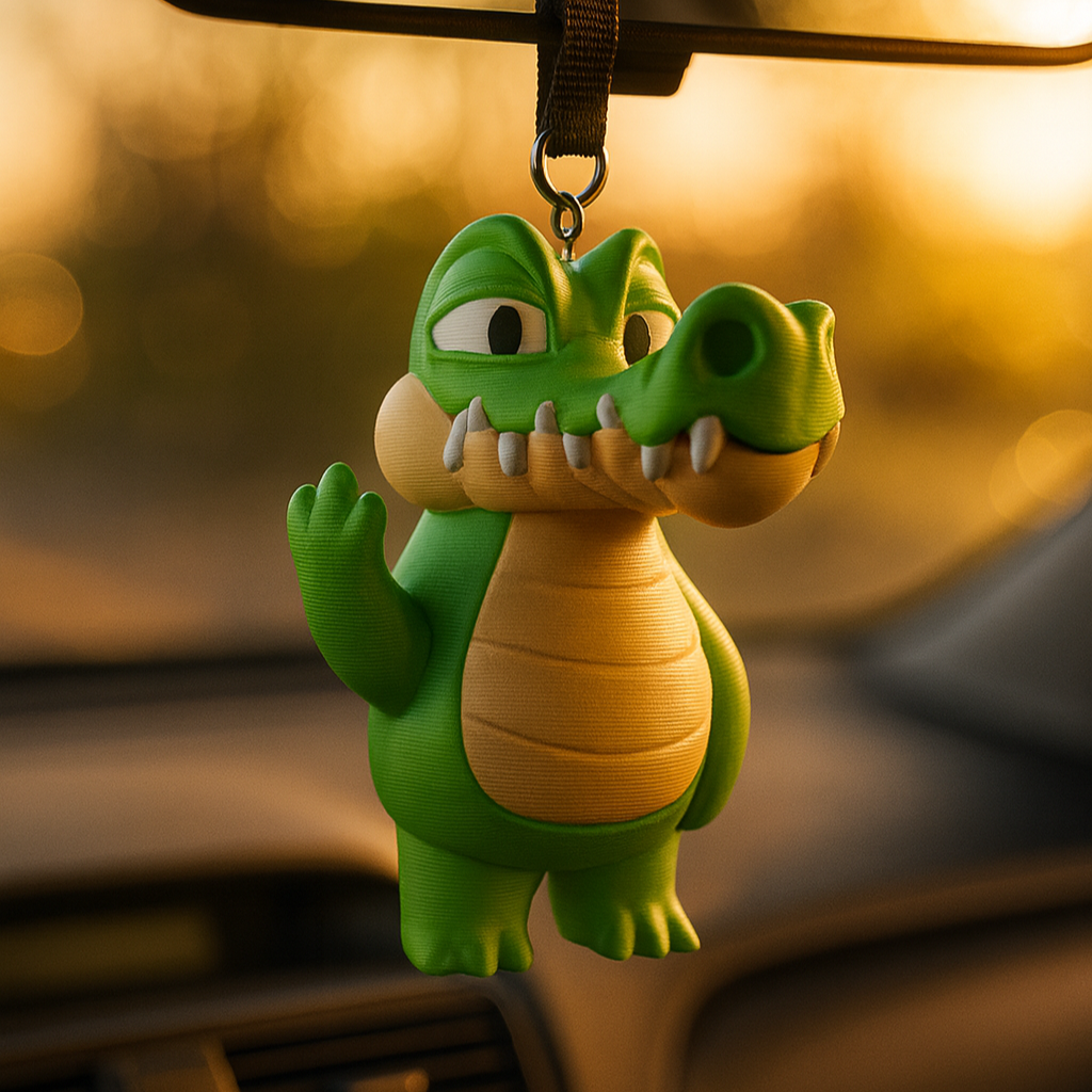 A playful green crocodile figurine with exaggerated cartoon features hangs from a car’s rearview mirror on a black strap. Its wide snout, large teeth, and cheeky raised hand gesture add humor and personality to the vehicle interior. The background glows with warm golden light from the setting sun, creating a vibrant and fun atmosphere. This decorative accessory combines quirky design with a lighthearted charm for drivers.